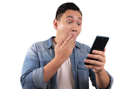Attractive young Asian man reading texting chatting  on his phone, shocked surprised expression