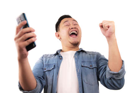 Attractive young Asian man have good news on his phone, smiling happy laughing winning expressionの写真素材