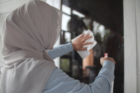 Muslim woman cleaning window glass with wag and spray, outdoor home windowの写真素材