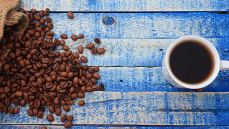 Roasted coffee beans and a glass of hot coffee, on blue wooden board with copy spaceの写真素材