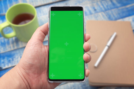 Close up image of smart phone mockup, phone with green screen template with working desk in the backgroundの写真素材