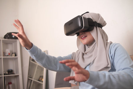Happy young Asian muslim woman wearing hijab playing on VR glasses. Virtual reality concept with a girl having fun with headset gogglesの写真素材