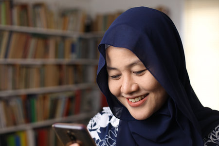 Asian muslim woman using phone and smiling. Feeling happy. Female doing communication on her smart phone, sending message or browsing onlineの写真素材