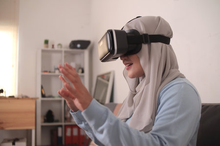 Happy young Asian muslim woman wearing hijab playing on VR glasses. Virtual reality concept with a girl having fun with headset gogglesの写真素材
