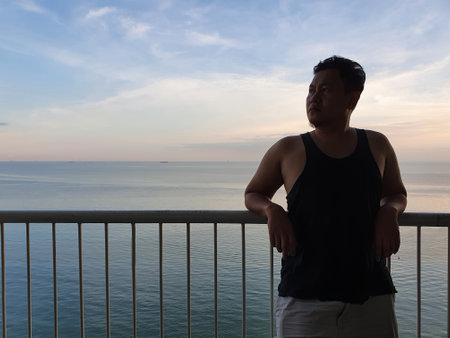 Silhouette of a man enjoys morning sunrise or sunset from his hotel balcony with calm blue ocean at the background, serene sceneの写真素材
