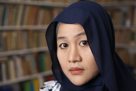 Portrait of Asian muslim woman wearing hijab looking at camera with book sell library on the backgroundの写真素材