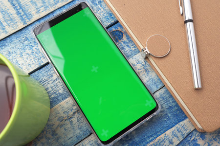 Close up image of smart phone mockup, phone with green screen template with working desk in the backgroundの写真素材