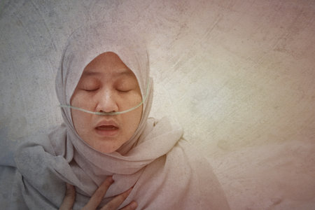 Asian muslim woman having asthma and hard to breathing.  patient in hospital suffer from respiratory disorder with oxygen tubing on her nose, grunge effect with copy spaceの写真素材