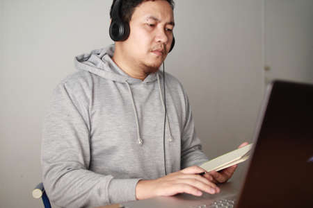 Asian man having video teleconference on his laptop at home, online learning or working from home conceptの写真素材