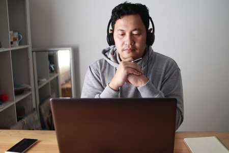 Asian man having video teleconference on his laptop at home, online learning or working from home conceptの写真素材