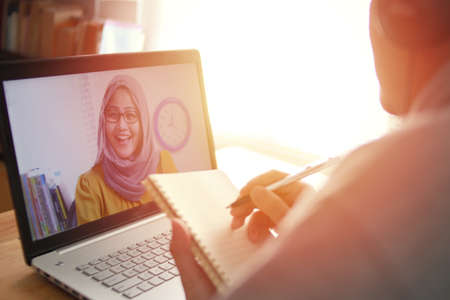Asian man having video teleconference with a woman on his laptop at home, online learning or working from home conceptの写真素材