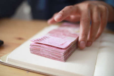 Close up of woman hand counting money uang Indonesian rupiah and making notes, money financial management conceptの写真素材