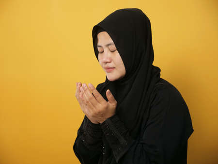 Portrait of mAsian muslim woman prays to God, praying gesture hands raised up, against yellow backgroundの写真素材