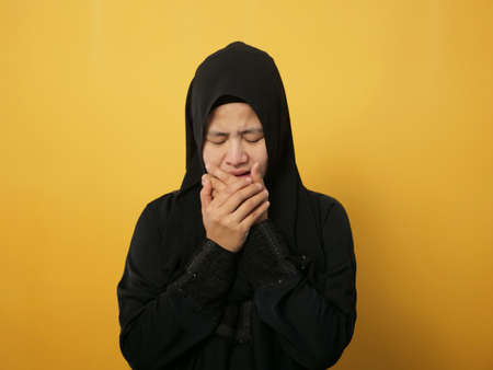Portrait of sad Asian muslim woman crying against yellow background, sadness depression hopeless conceptの写真素材