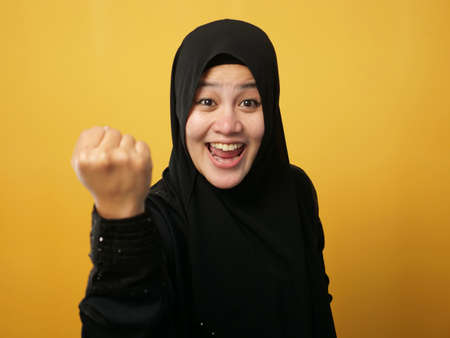 Portrait of success beautiful muslim businesswoman wearing hijab screaming shouting and shows winning victory gesture over yellow backgroundの写真素材