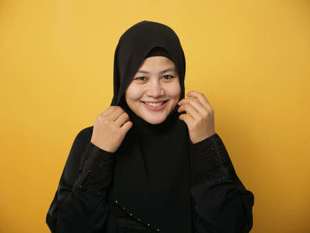 Portrait of beautiful Asian muslim woman wearing hijab smiling at camera, against yellow backgroundの写真素材