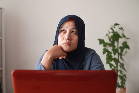 Portrait of Asian muslim woman thinking contemplationg while working on her laptop, sad emotion expressionの写真素材