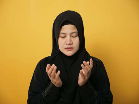 Portrait of mAsian muslim woman prays to God, praying gesture hands raised up, against yellow backgroundの写真素材