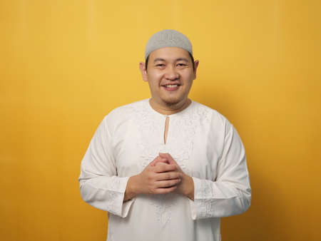 Portrait of happy young Asian muslim man smiling and posing for camera, against yellow backgroundの写真素材