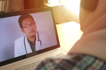 Concept of online medical healthcare services, muslim woman doing video call with male doctor, telehealth, telemedicine consultationの写真素材