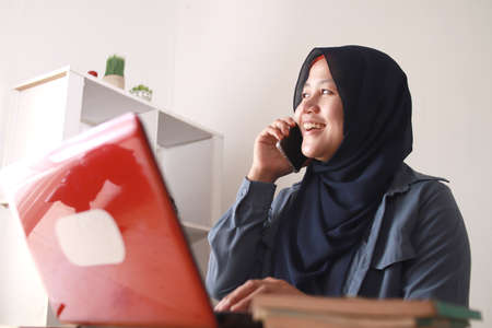 Portrait of happy Asian muslim businesswoman female entrepreneur making business phone call while...