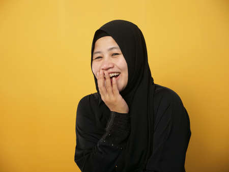 Portrait of muslim lady wearing hijab laughing to see somwthing funny, happy cheerful expression, against yellow backgroundの写真素材