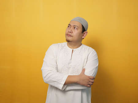 Asian muslim man shows thinking contemplating expression. Looking for solution of a problem. Close up portrait against yellow backgroundの写真素材