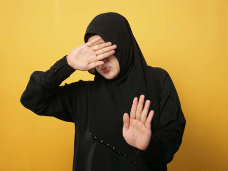 Portrait of beautiful Asian musim woman afraid expression with hands raised up, surrender gesture, over yellow backgroundの写真素材