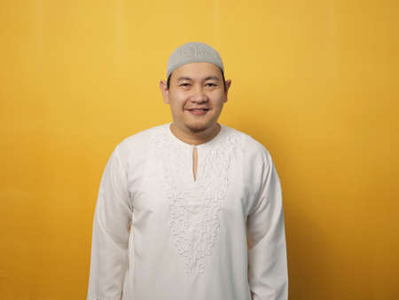 Portrait of happy young Asian muslim man smiling and posing for camera, against yellow backgroundの写真素材