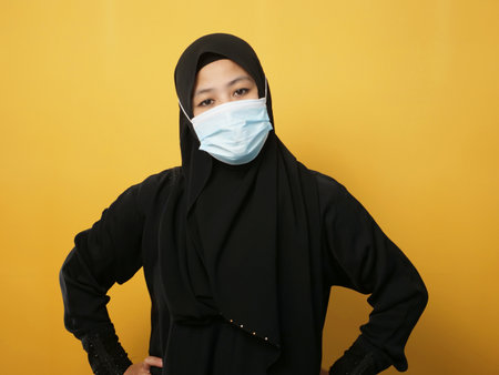 Asian muslim woman wearing hijab and mask during  pandemic new normal, woman wearing face protective mask, against yellow backgroundの写真素材