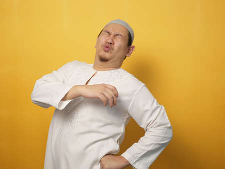 Portrait of young Asian muslim man having lower back pain, against yellow background