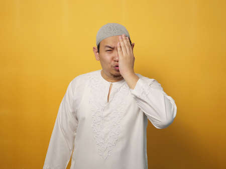 Asian muslim man looking at camera with sad and regret expression, disappointed upset gesture, against yellow backgroundの写真素材