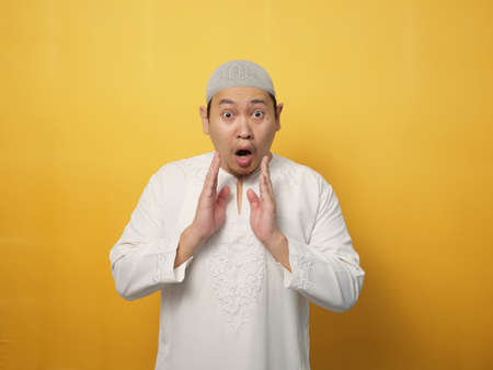 Young asian muslim man shocked gesture can not believe of what he sees. Worried expression, against yellow backgroundの写真素材