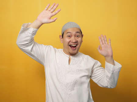 Funny young Asian muslim man dancing happily joyful expressing celebrating good news victory winning success gesture, smiling positive excited emotion, against yellow backgroundの写真素材