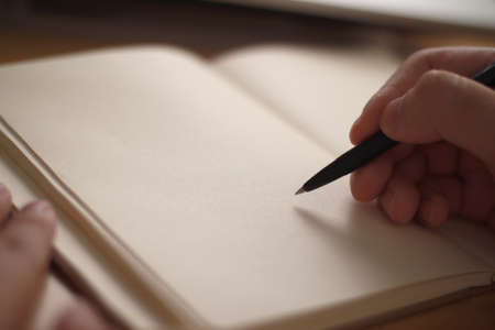 Close up of hand holding pen and writing on empty book paper, selective focus on penの写真素材