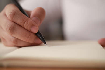 Close up of hand holding pen and writing on empty book paper, selective focus on penの写真素材