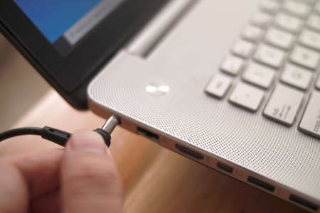 Close up of a person inserting power cord to laptop, charging laptopの写真素材