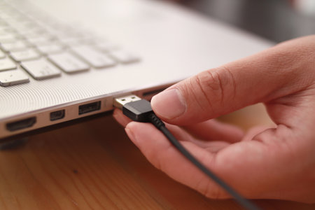 Close up of hand inserting plugging data cable into usb port in laptop, data transfer concept