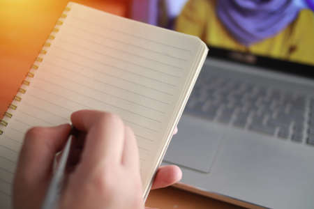 Hand of a student writing on empty notebook, with laptop in the background. Online education class conceptの写真素材