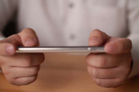 Close up of adult person hands holding and using smart phone to play online game. Leisure activity in spare timeの写真素材