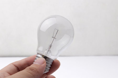 Hand holding vintage retro filament lamp light bulb against white tableの写真素材