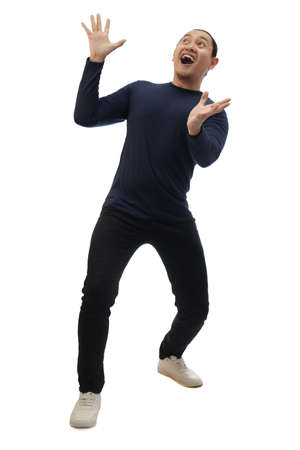 Man wearing casual blue shirt black denim and white shoes, excited surprised shocked and happy anticipating something amazing from above. Full body portrait isolated cut outの写真素材