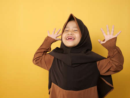 Funny cute Asian muslim little girl wearing hijab looked happy and laughing, against yellow backgroundの写真素材