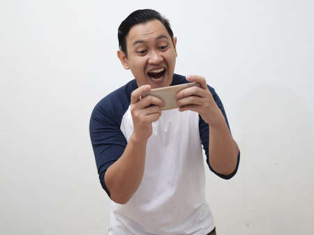 Happy young Asian man with funny face playing games on tablet smart phoneの写真素材