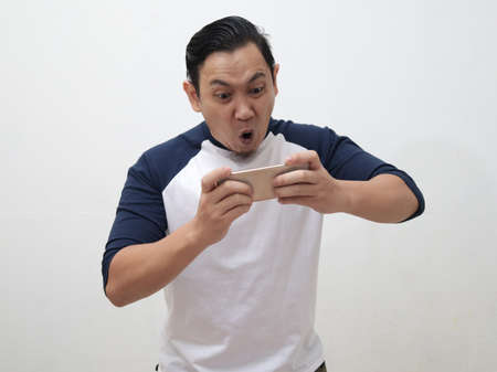 Happy young Asian man with funny face playing games on tablet smart phoneの写真素材