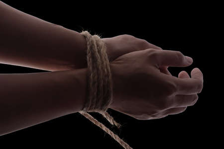 Person hands tied with rope isolated on black dark background, captive victim restrained conceptの写真素材