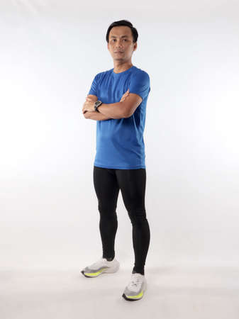 Strong confidence athletic young Asian male wearing running jersey looking at camera with crossed arms, full length studio shot portrait against white backgroundの写真素材