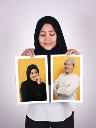 Asian muslim woman wearing hijab smiling and holding to shows picture of herself and her man, happy couple conceptの写真素材