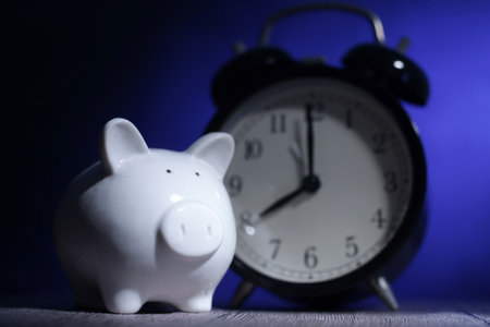 Piggybank and alarm clock, concept of investment money management and time relation. Under blue lightの写真素材