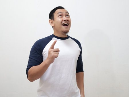 Young Asian man looked happy thinking and looking up, having good idea. Half body portrait against white wall with copy spaceの写真素材